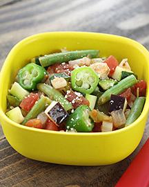 A salad of sliced green peppers, green beans, tomatoes and eggplant in a yellow bowl.
