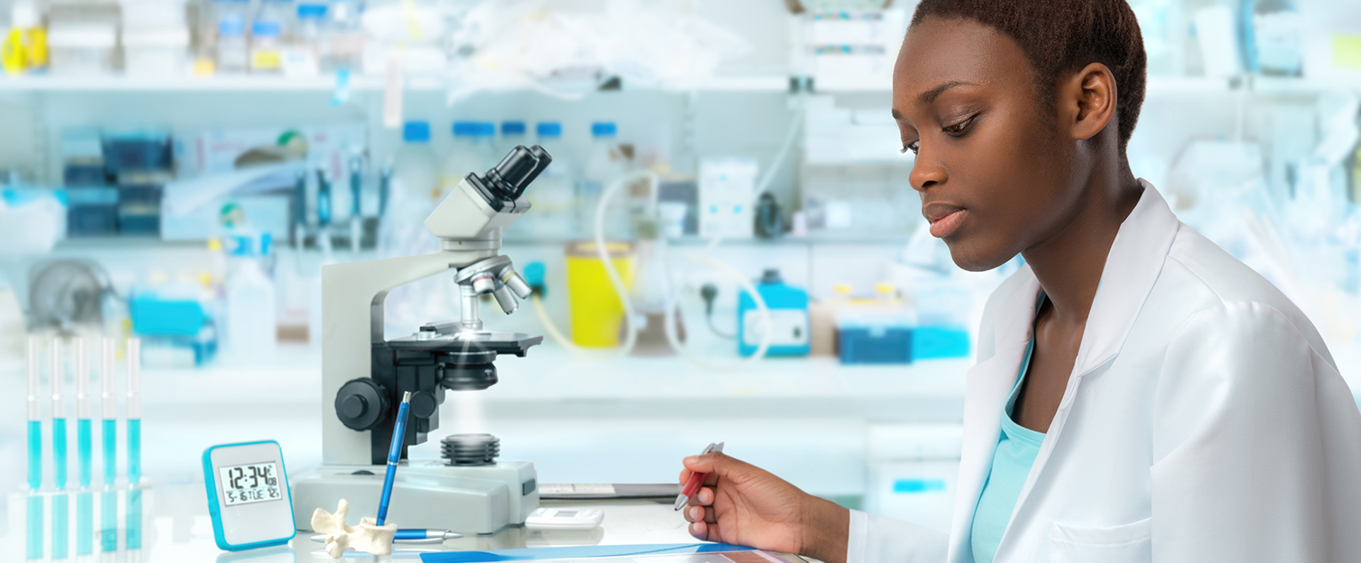 Female in a white lab coat sitting in front of a microscope in a laboratory
