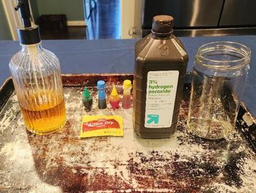 bottle of hydrogen, dry yeast, dish soap, food coloring, warm water, cookie sheet, measuring cups, and safety glasses