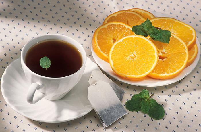 A cup of hot tea with a sprig of mint and plate of sliced oranges.