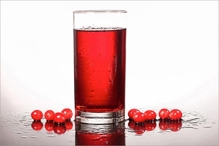 A glass of cranberry juice surrounded by several fresh whole cranberries. 