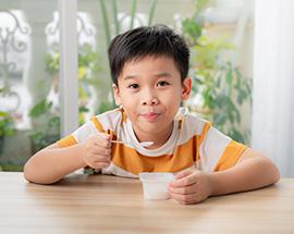 A young Asian boy eating yogurt