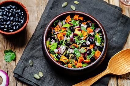 A bowl of black beans next to a salad of roasted sweet potatoes, black beans, pumpkin seeds and avocado.