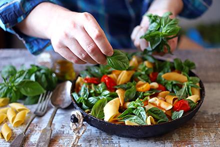 Person adding basil to pasta dish.