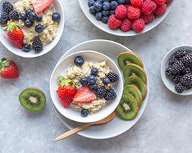 Two bowls of oatmeal topped with blueberries and strawberries surrounded by sliced kiwi fruit. 