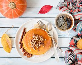 Breakfastfueling Pumpkin pancakes with pecan nuts, honey and cup of coffee on white table.