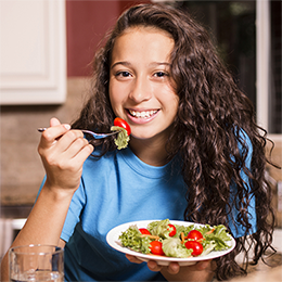 A young girl wearing a blue shirt and eating a plate of salad.