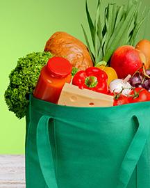 A reusable shopping bag filled with apples, peppers, a loaf of bread, a head of broccoli, an onion and grapes