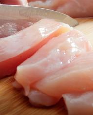 A knife slicing raw chicken