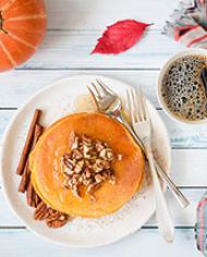 Pumpkin pancakes with pecan nuts, honey and cup of coffee on white table. 