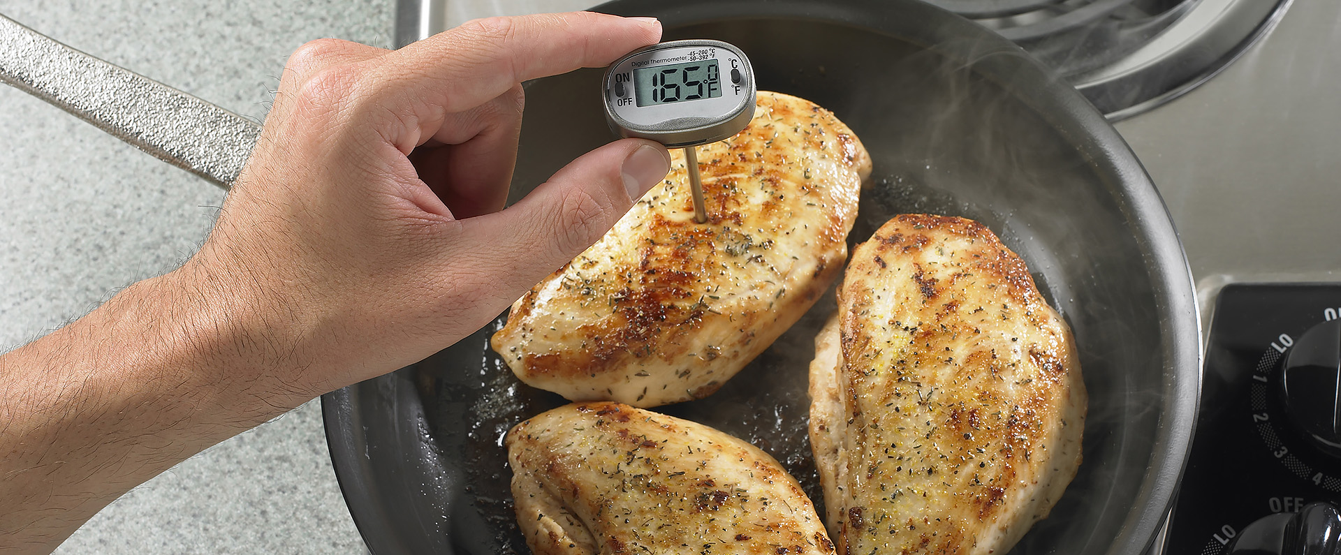 A hand holding a thermometer in a chicken thigh to check the temperature. 