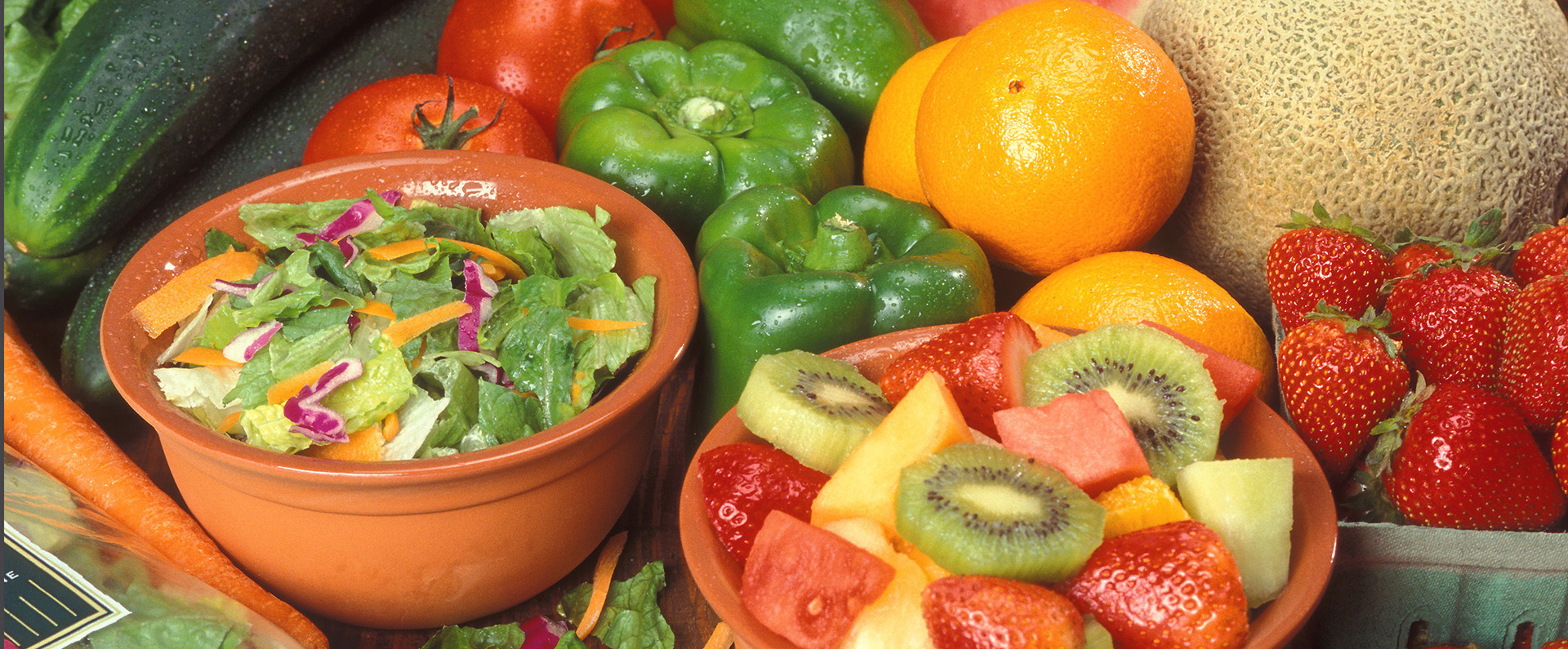 Oranges, cantaloupe, green peppers and tomatoes beside a bowl of salad, a bowl of fresh fruits and a basket of strawberries.